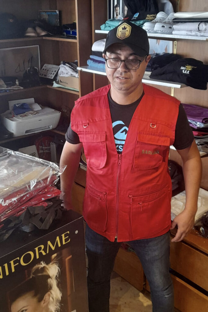 Homme en gilet multipoches rouge et casquette dans le magasin Good Uniforme